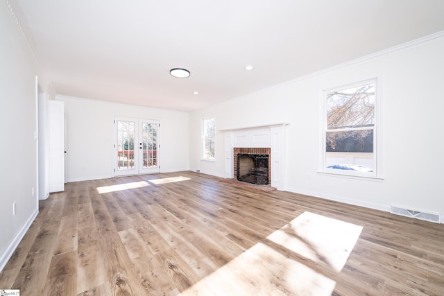 unfurnished living room featuring french doors, light wood-type flooring, crown molding, and a brick fireplace