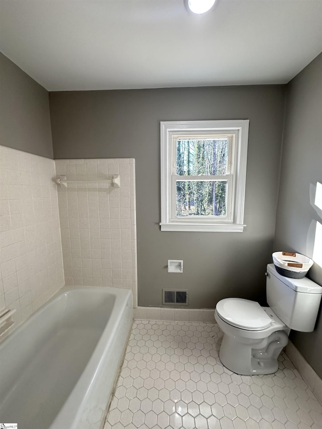 bathroom with toilet, visible vents, baseboards, a bath, and tile patterned floors