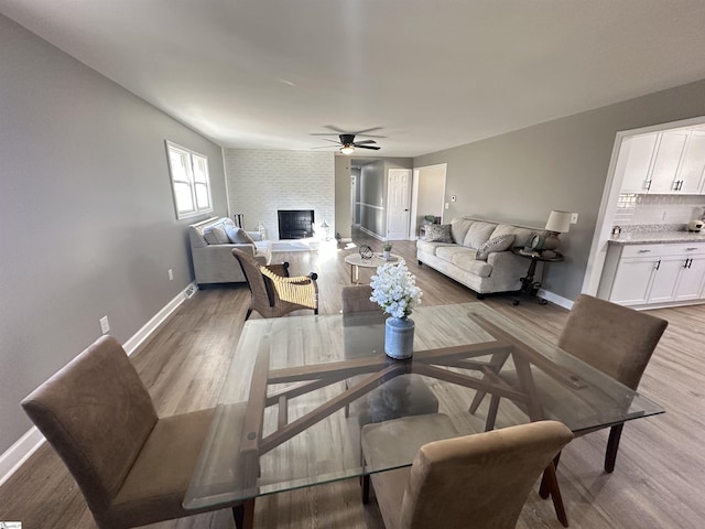 living area with a brick fireplace, light wood-style flooring, baseboards, and ceiling fan