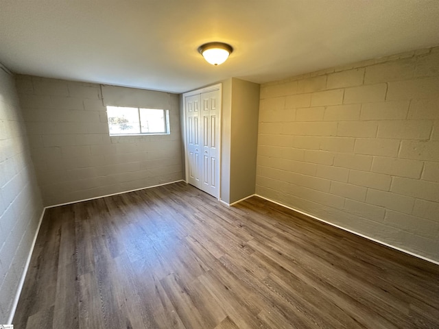 unfurnished bedroom with concrete block wall, a closet, and wood finished floors