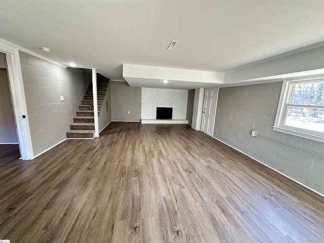 unfurnished living room with dark wood-type flooring, concrete block wall, a fireplace, and stairway