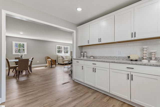 kitchen featuring light wood finished floors, tasteful backsplash, visible vents, white cabinets, and light stone counters