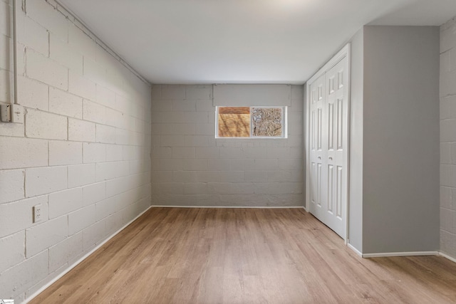 empty room with light wood-style flooring and concrete block wall