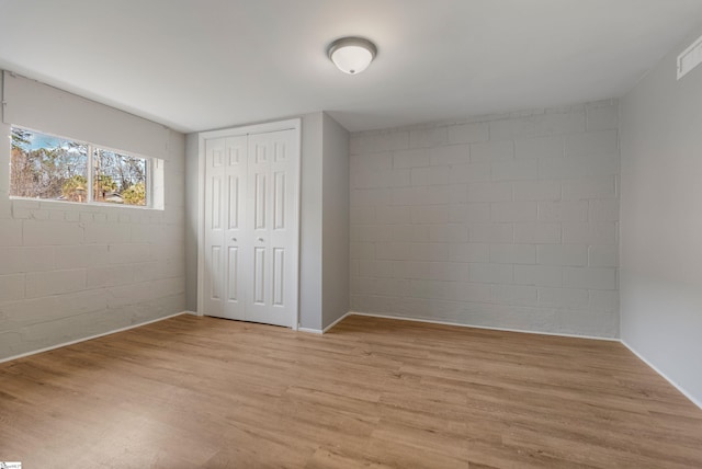 unfurnished bedroom featuring a closet, light wood-style flooring, and concrete block wall