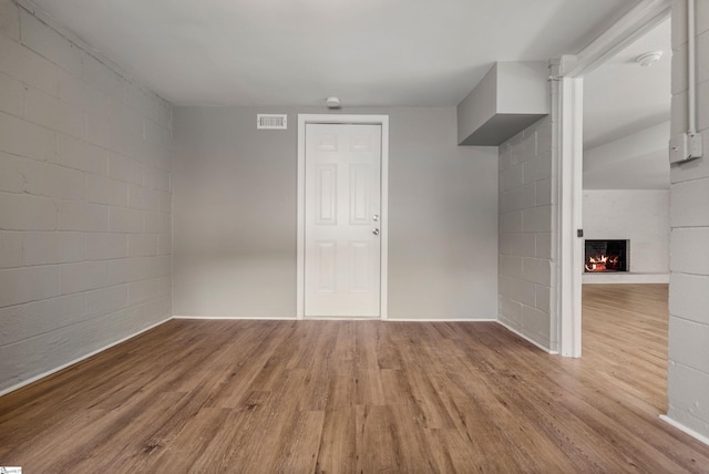 spare room featuring a warm lit fireplace, wood finished floors, visible vents, and concrete block wall