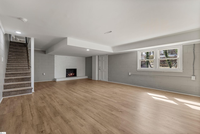 unfurnished living room with light wood finished floors, stairway, a brick fireplace, and concrete block wall