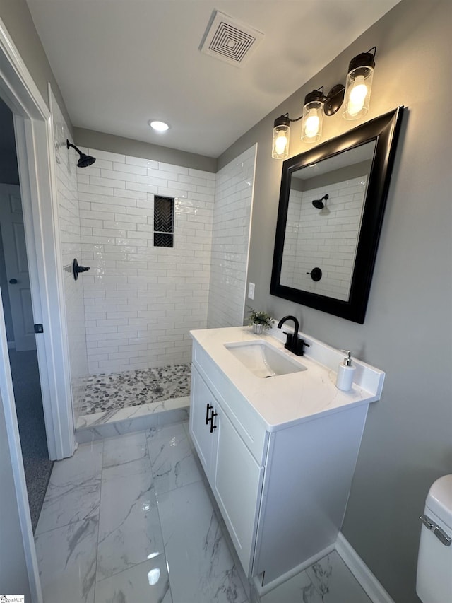 bathroom with toilet, vanity, visible vents, marble finish floor, and a tile shower