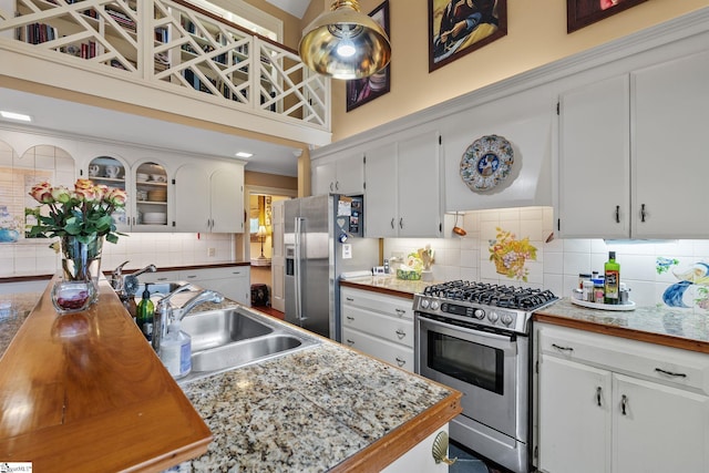 kitchen with white cabinetry, sink, tasteful backsplash, a towering ceiling, and appliances with stainless steel finishes