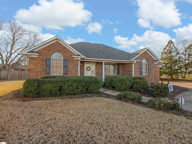 ranch-style home featuring brick siding, a front yard, roof with shingles, and fence