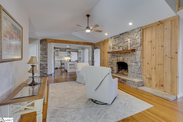 living room with vaulted ceiling, light hardwood / wood-style floors, a stone fireplace, and ceiling fan