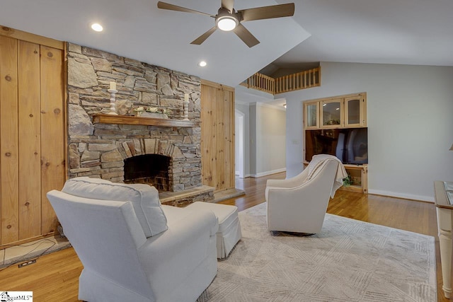 living room featuring a stone fireplace, ceiling fan, light hardwood / wood-style flooring, and vaulted ceiling