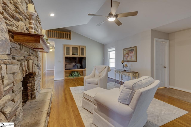 living room with vaulted ceiling, light hardwood / wood-style flooring, a stone fireplace, and ceiling fan