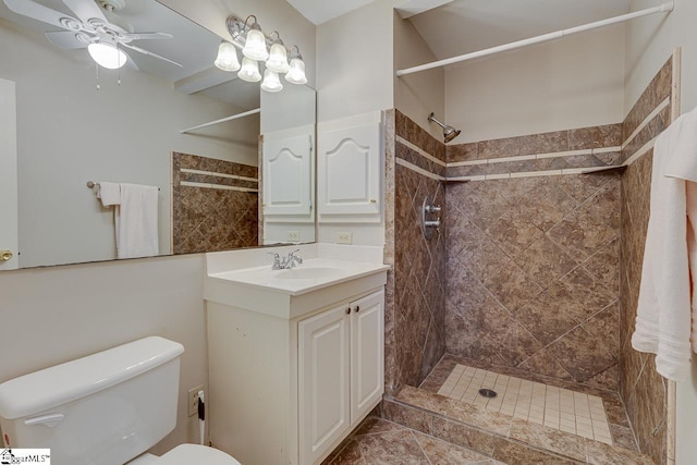 bathroom with a tile shower, vanity, toilet, and ceiling fan