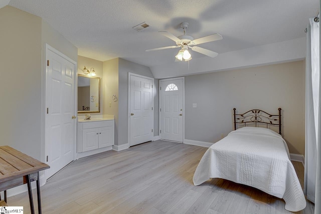 bedroom featuring ensuite bathroom, a textured ceiling, ceiling fan, light hardwood / wood-style flooring, and lofted ceiling