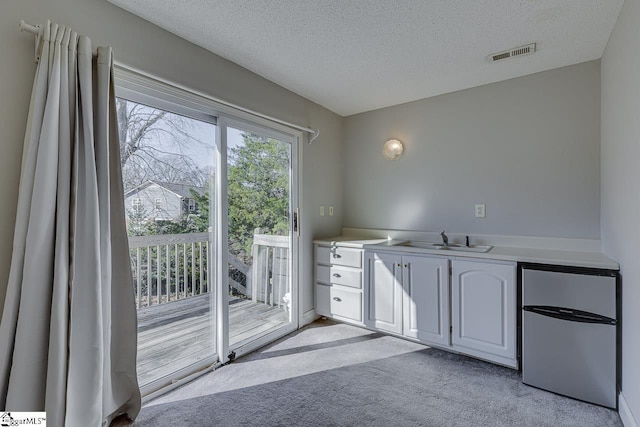 kitchen with white cabinetry, sink, a textured ceiling, fridge, and light carpet