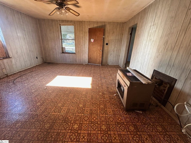 empty room featuring heating unit, ceiling fan, and wooden walls