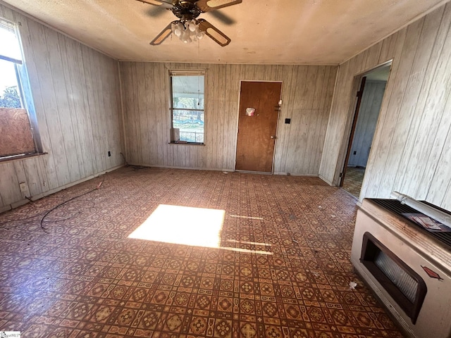 spare room with a textured ceiling, heating unit, ceiling fan, and wood walls