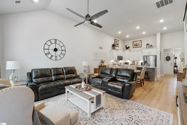 living room with light hardwood / wood-style floors, vaulted ceiling, and ceiling fan