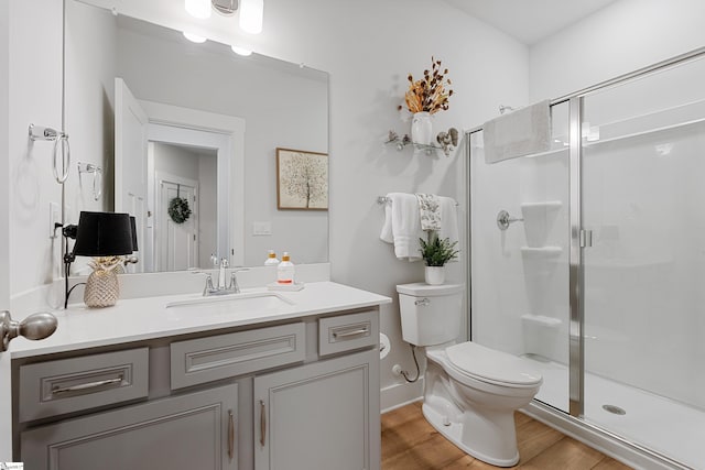 bathroom featuring wood-type flooring, vanity, toilet, and a shower with shower door