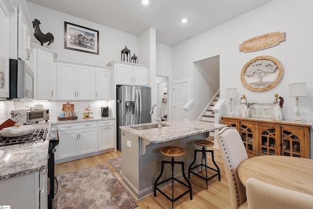 kitchen with white cabinetry, sink, light stone countertops, a center island with sink, and appliances with stainless steel finishes