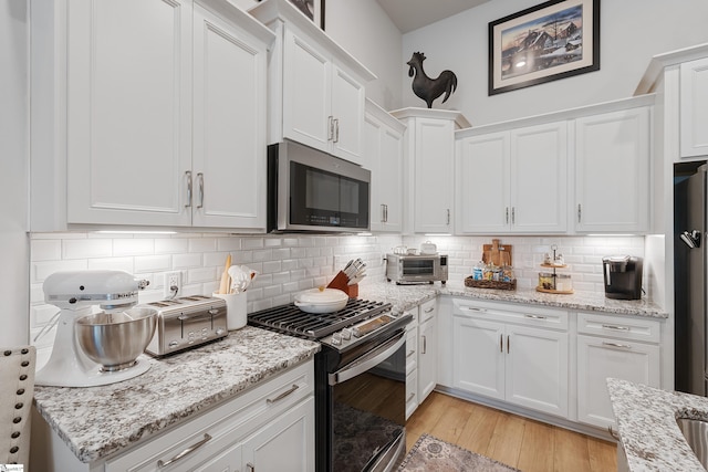 kitchen featuring appliances with stainless steel finishes, backsplash, light hardwood / wood-style floors, and white cabinetry