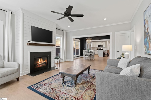 living room with a large fireplace, ceiling fan, light hardwood / wood-style flooring, and ornamental molding