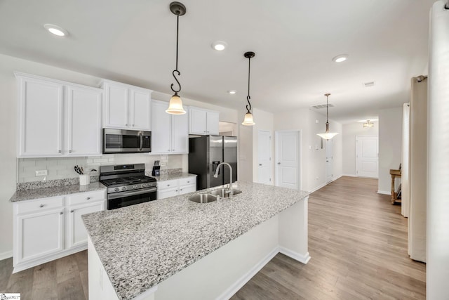 kitchen with appliances with stainless steel finishes, sink, decorative light fixtures, white cabinets, and an island with sink