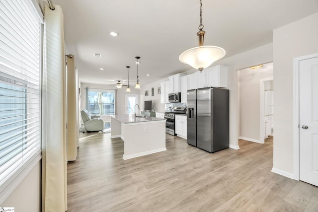 kitchen with white cabinetry, light stone counters, pendant lighting, a center island with sink, and appliances with stainless steel finishes