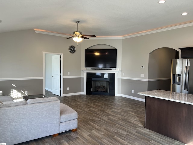 unfurnished living room featuring ornamental molding, ceiling fan, dark wood-type flooring, a tile fireplace, and lofted ceiling