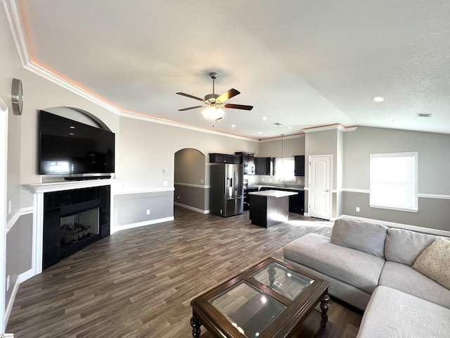 living room with lofted ceiling, crown molding, ceiling fan, dark hardwood / wood-style flooring, and a tiled fireplace