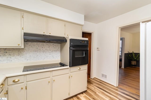 kitchen with backsplash, cream cabinetry, black appliances, and light wood-type flooring