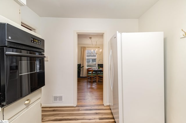 kitchen featuring white refrigerator, an inviting chandelier, black oven, and light hardwood / wood-style floors