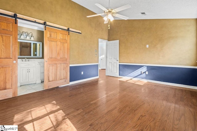 unfurnished room featuring ceiling fan, a barn door, light hardwood / wood-style flooring, a textured ceiling, and vaulted ceiling