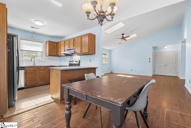 kitchen featuring light stone countertops, light wood-type flooring, vaulted ceiling with skylight, ceiling fan with notable chandelier, and stainless steel appliances