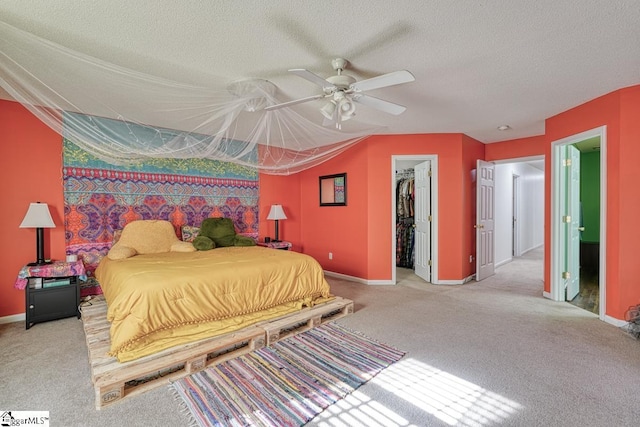 carpeted bedroom featuring a walk in closet, ceiling fan, a closet, and a textured ceiling