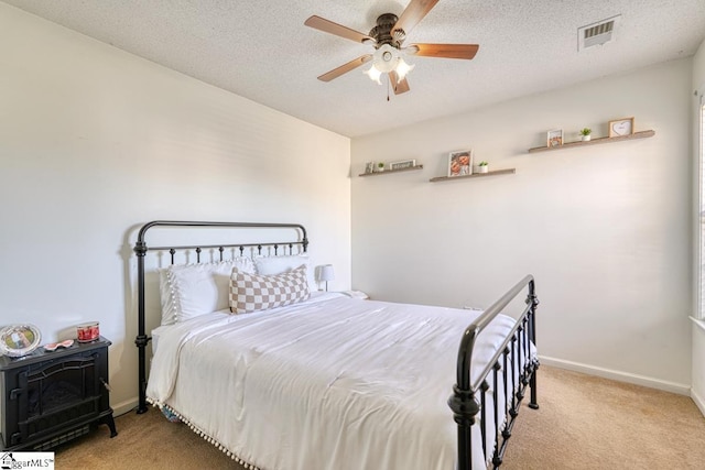 bedroom with ceiling fan, light colored carpet, and a textured ceiling