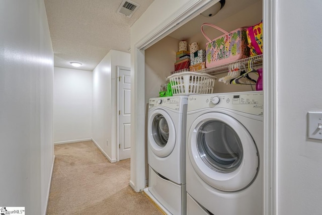 washroom featuring washing machine and clothes dryer, light carpet, and a textured ceiling