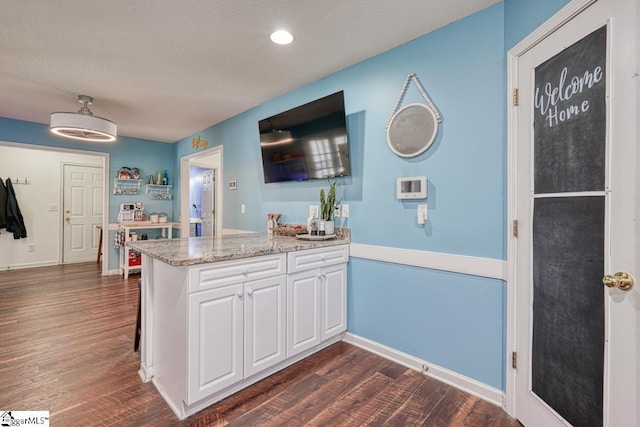 kitchen featuring dark hardwood / wood-style floors, light stone countertops, white cabinetry, and kitchen peninsula