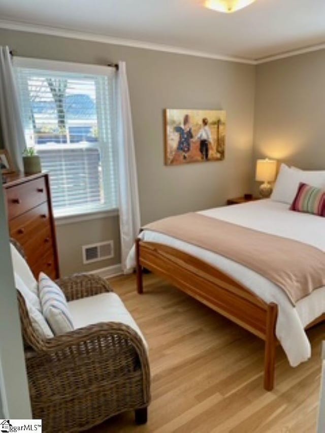 bedroom featuring wood-type flooring, ornamental molding, and multiple windows