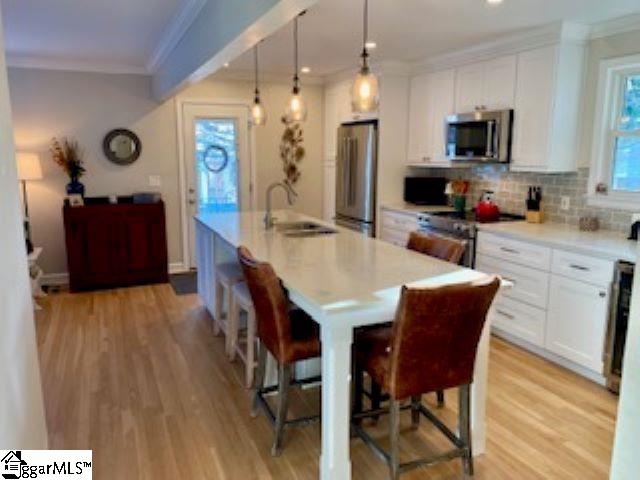 kitchen featuring white cabinetry, sink, stainless steel appliances, a breakfast bar area, and a kitchen island with sink