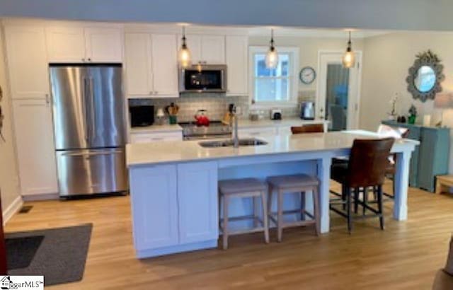 kitchen with sink, pendant lighting, white cabinetry, stainless steel refrigerator, and an island with sink