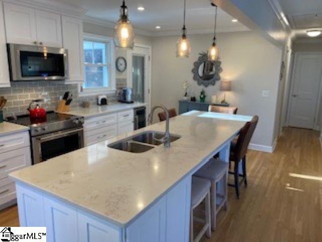 kitchen featuring a kitchen island with sink, sink, white cabinets, and stainless steel appliances