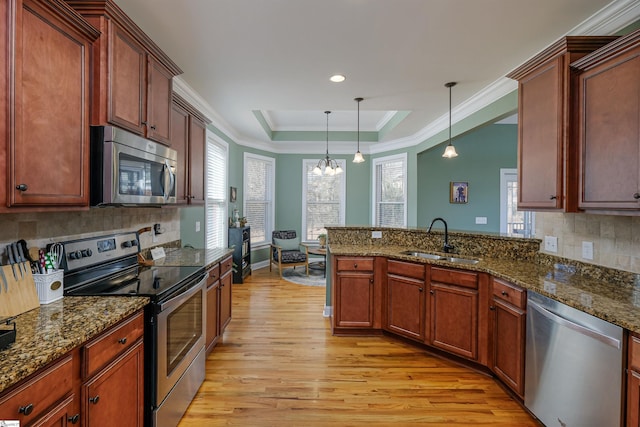 kitchen with sink, stainless steel appliances, dark stone countertops, decorative light fixtures, and a tray ceiling