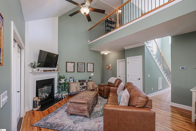 living room with ceiling fan, a high ceiling, and light wood-type flooring