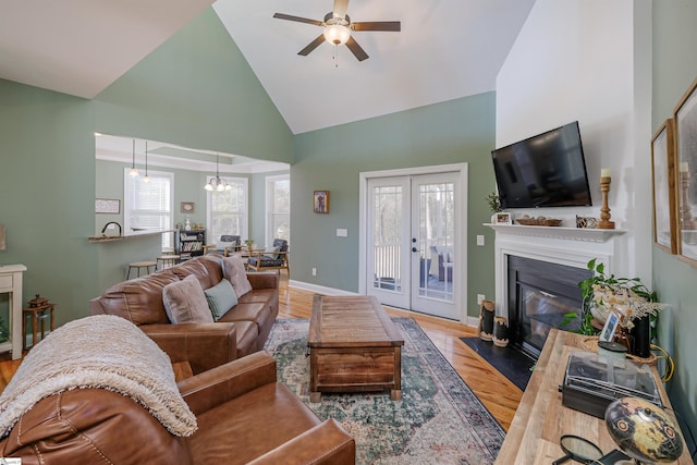 living room with french doors, light hardwood / wood-style flooring, high vaulted ceiling, and ceiling fan with notable chandelier