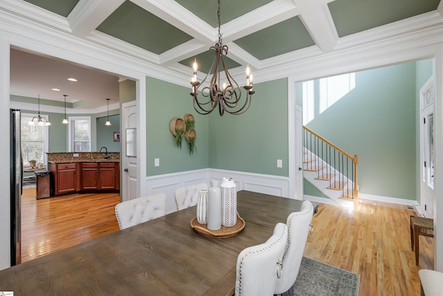 dining area featuring an inviting chandelier, coffered ceiling, sink, ornamental molding, and light hardwood / wood-style floors