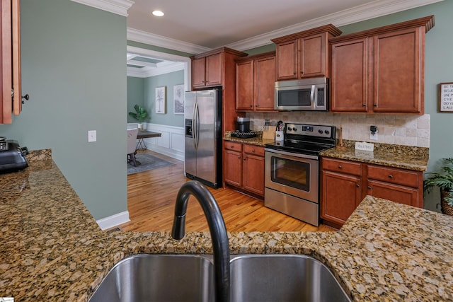 kitchen featuring sink, ornamental molding, appliances with stainless steel finishes, stone countertops, and light hardwood / wood-style floors