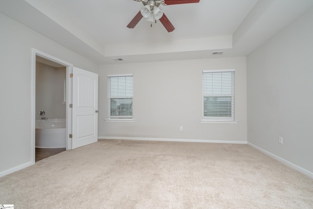 unfurnished bedroom with ceiling fan, ensuite bathroom, a raised ceiling, and carpet floors