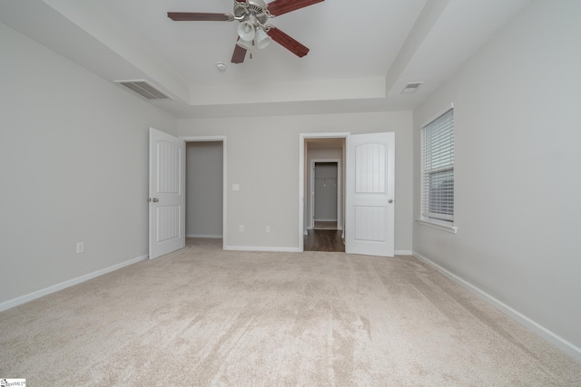 unfurnished bedroom with ceiling fan, a tray ceiling, and carpet flooring