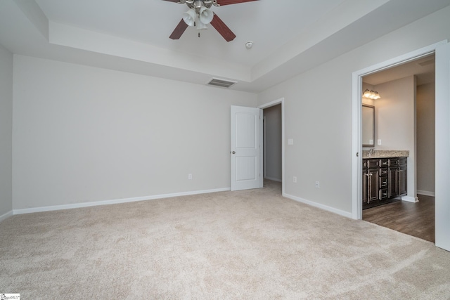 unfurnished bedroom with ensuite bath, ceiling fan, a tray ceiling, and carpet flooring